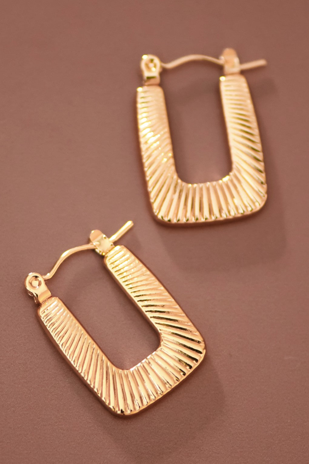 Textured gold hoop earrings on a brown background