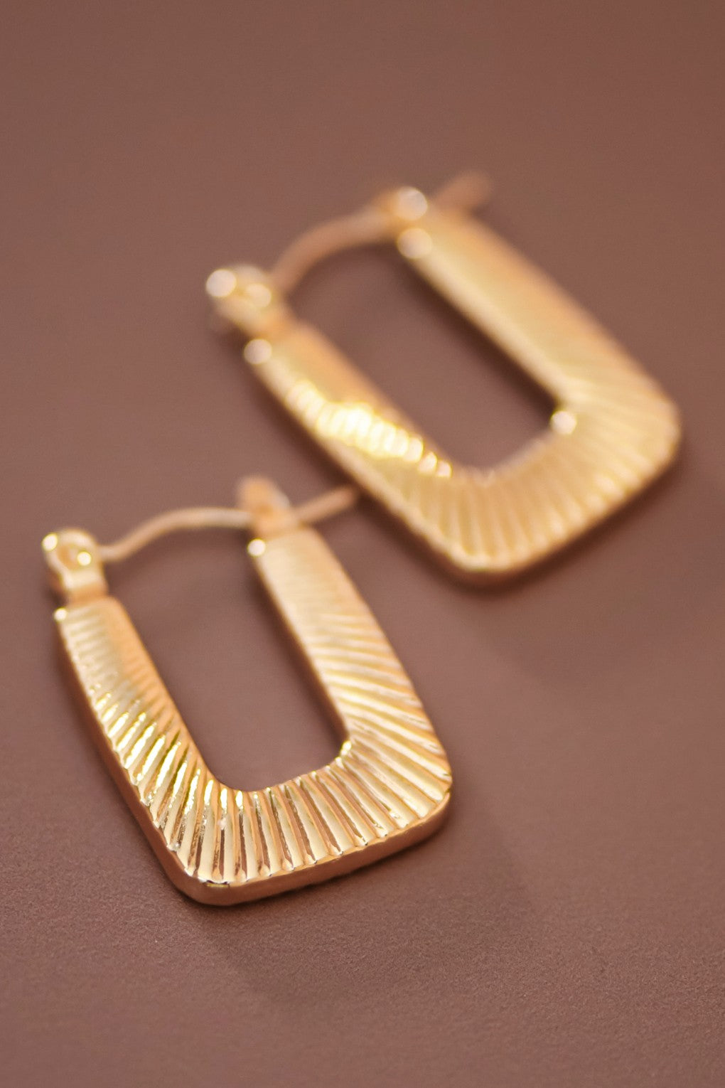 Textured gold hoop earrings on a brown background