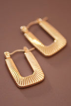Textured gold hoop earrings on a brown background