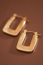 Textured gold hoop earrings on a brown background
