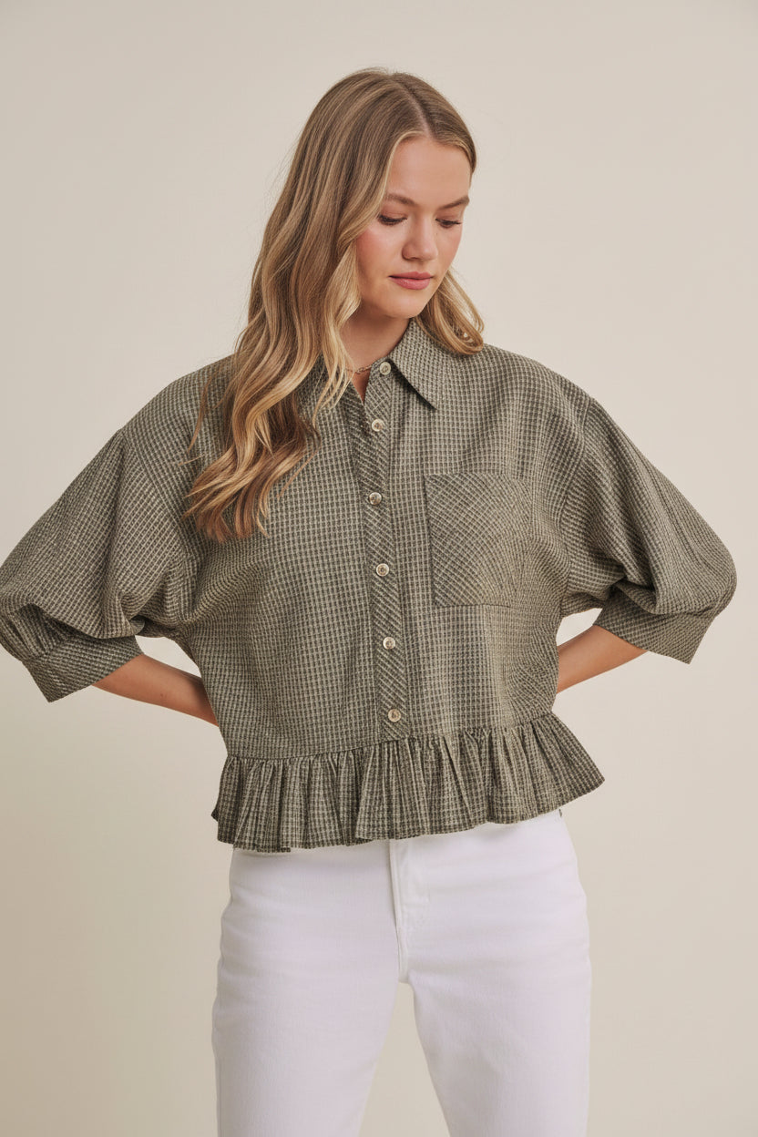 Woman wearing an olive micro check blouse with puff sleeves and ruffle hem on a beige background