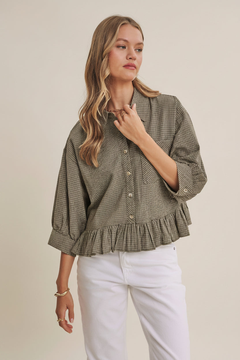 Woman wearing an olive micro check blouse with puff sleeves and ruffle hem on a beige background