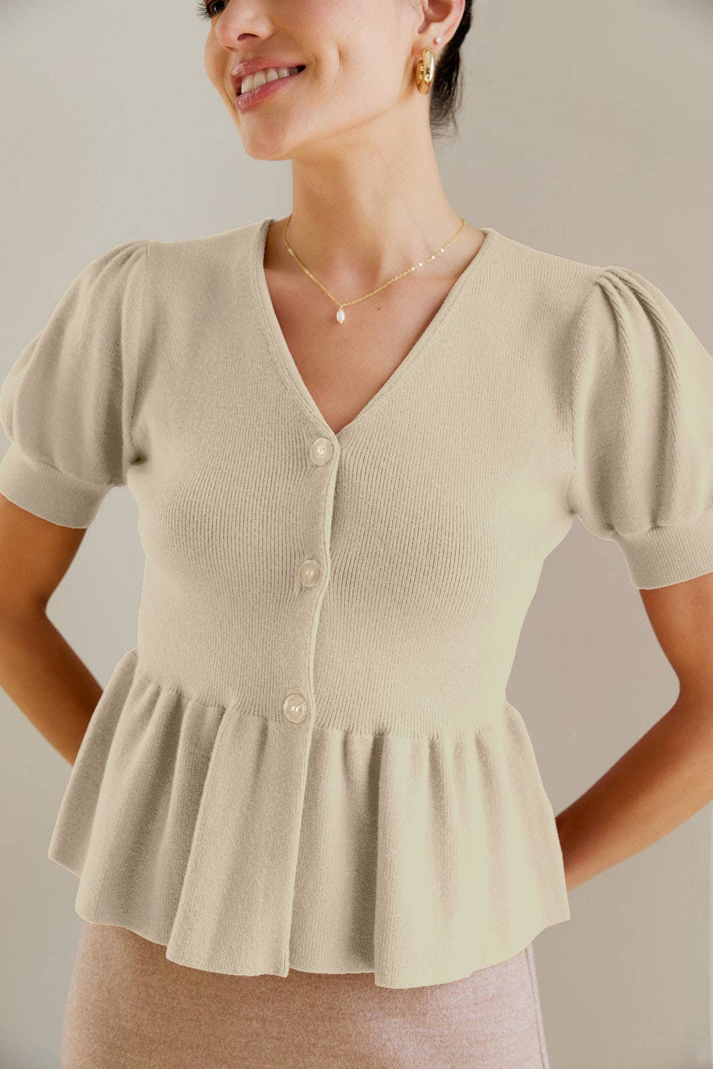 Woman wearing a cream knit button peplum top with puffed sleeves against a neutral background