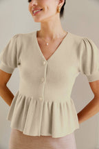 Woman wearing a cream knit button peplum top with puffed sleeves against a neutral background