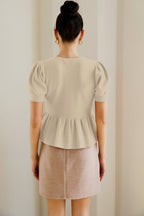 Woman wearing a cream button  peplum top against a plain background