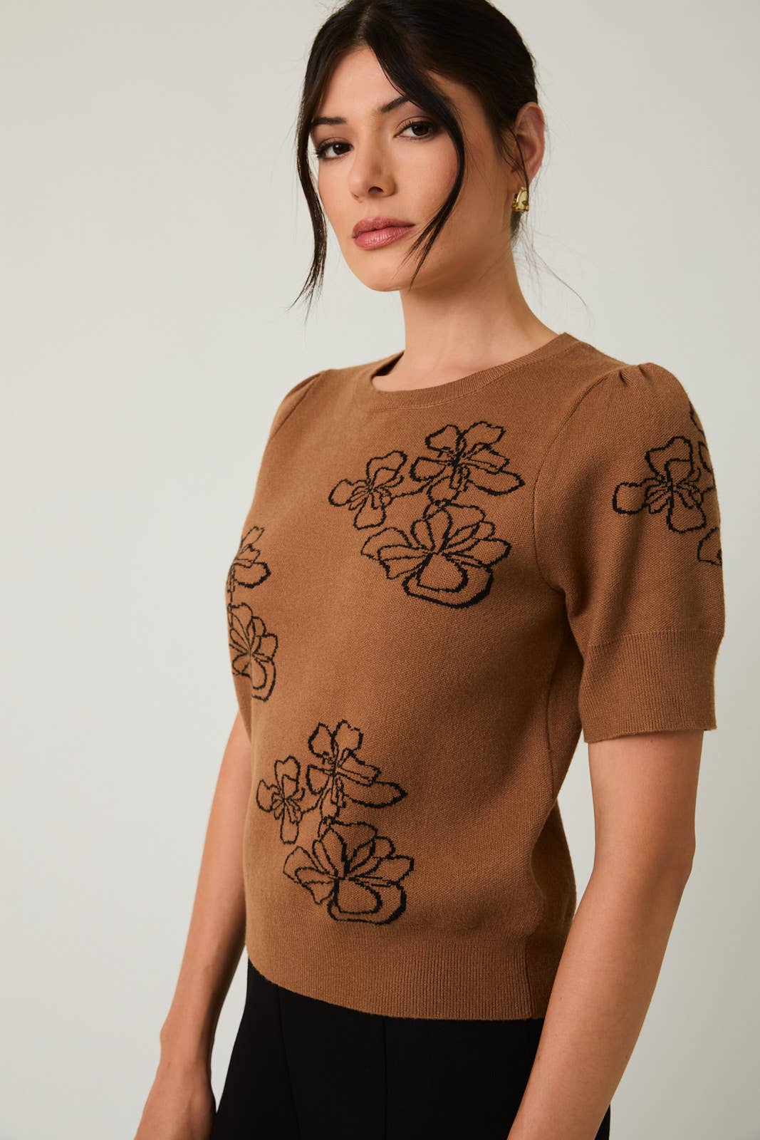 Woman wearing a brown sweater with black flower design on a plain background