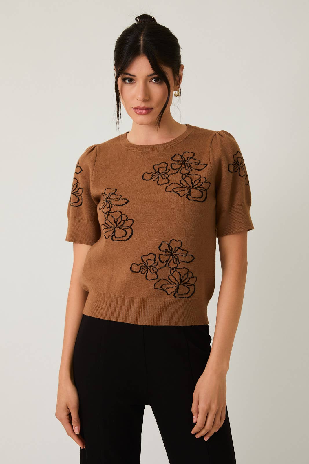 Woman wearing a brown sweater with black flower design on white background