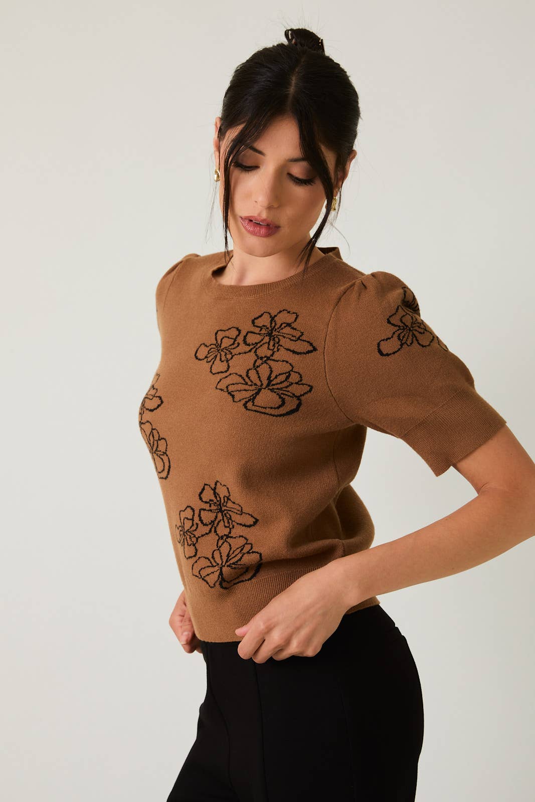 Woman wearing a brown sweater with black flower design on a plain background