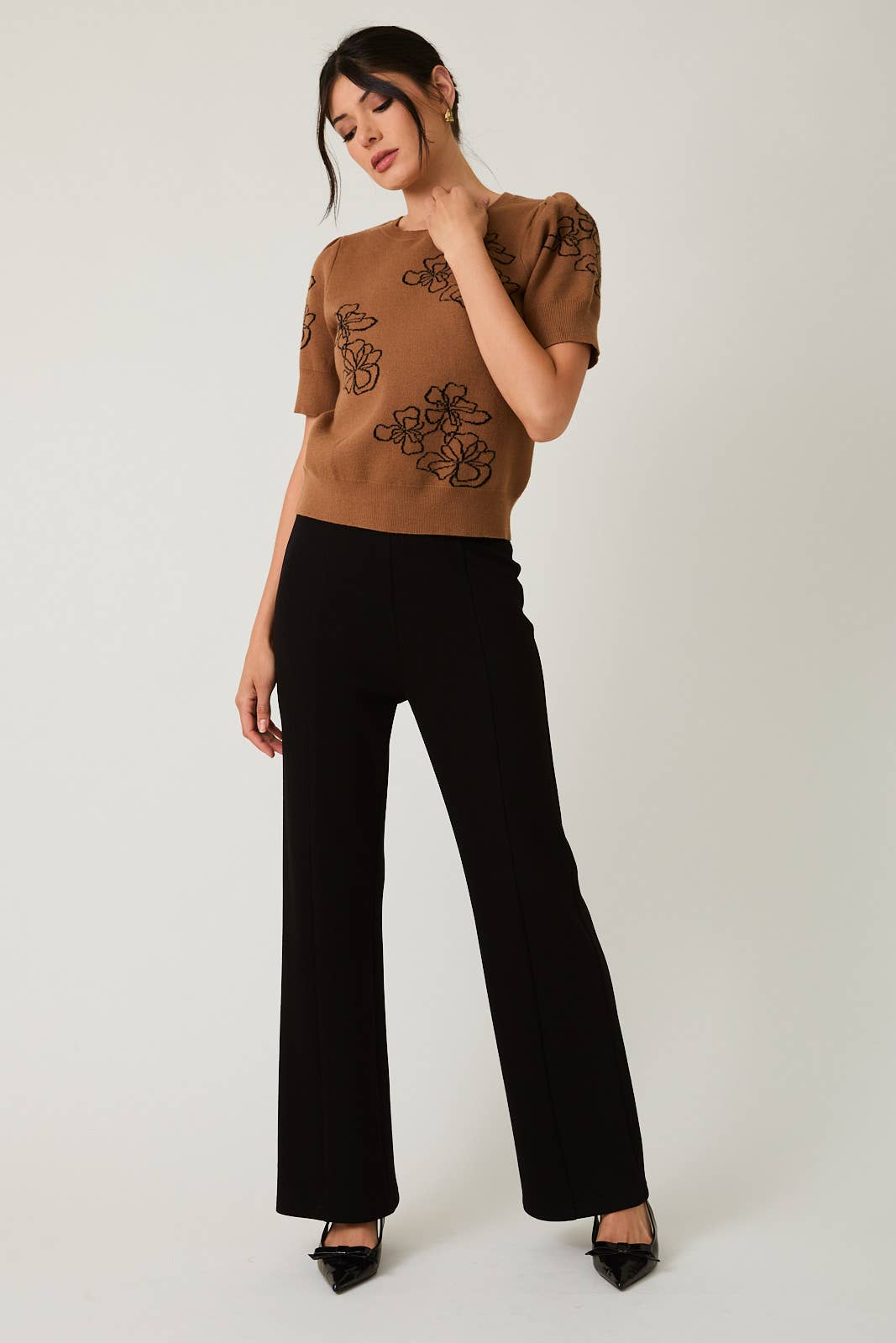 Woman wearing a brown top with black flower design and black pants on a white background