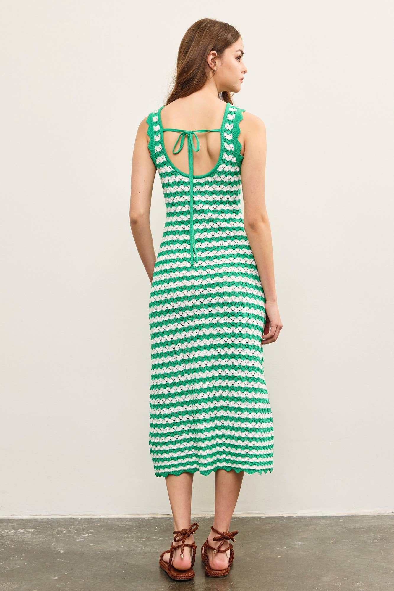 Back view of a woman wearing a green and white wavy striped tank midi dress against a plain background