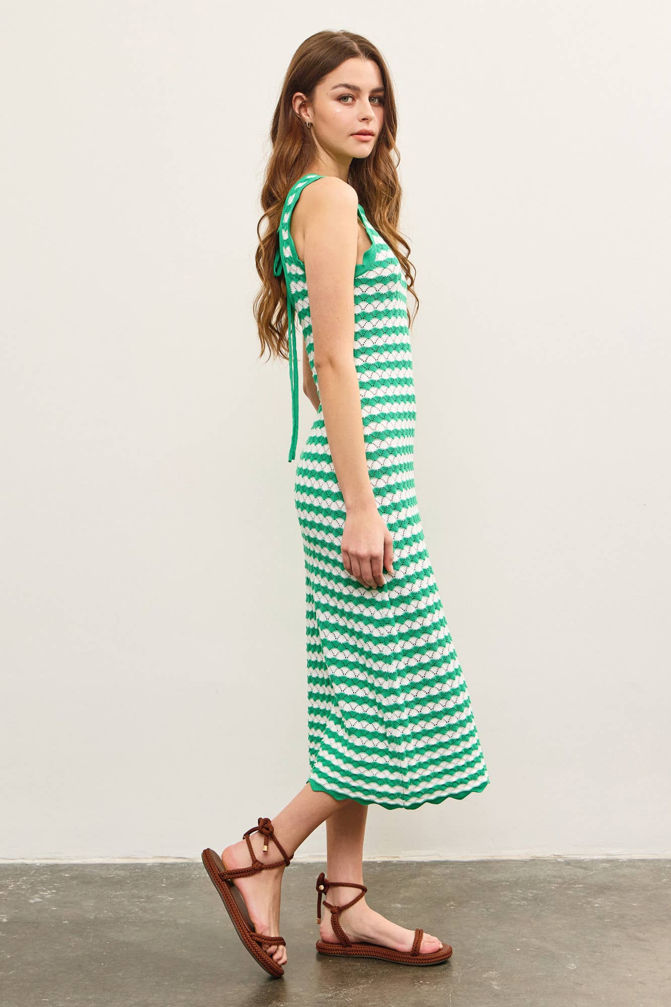 Woman wearing a green and white wavy striped tank midi dress against a plain background