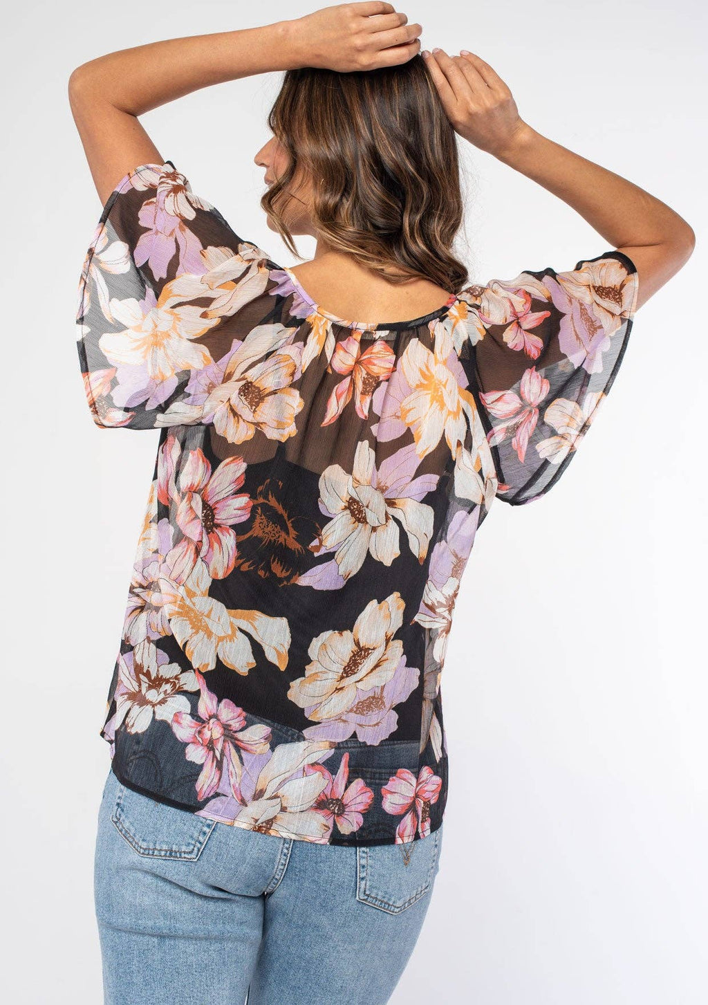 Back view of a woman wearing a floral blouse with a plain background