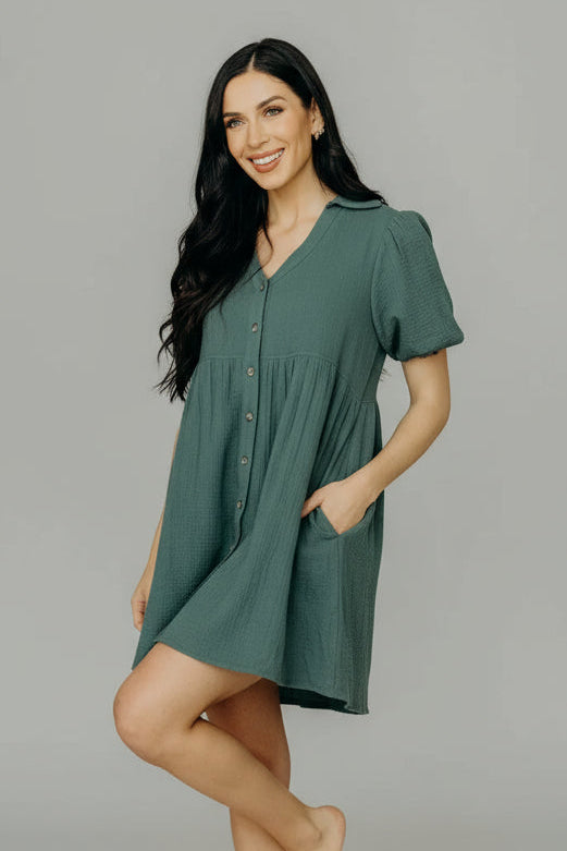 Woman in a green bubble sleeve dress standing in a room with a chair and cabinet.