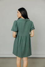 Woman wearing a green bubble sleeve dress standing in a room with a couch and decor.