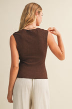 Back view of a woman wearing a brown bubble texture sleeveless top and white pants against a beige background