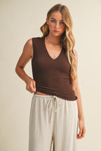 Woman wearing a brown bubble texture sleeveless top and white pants against a beige background
