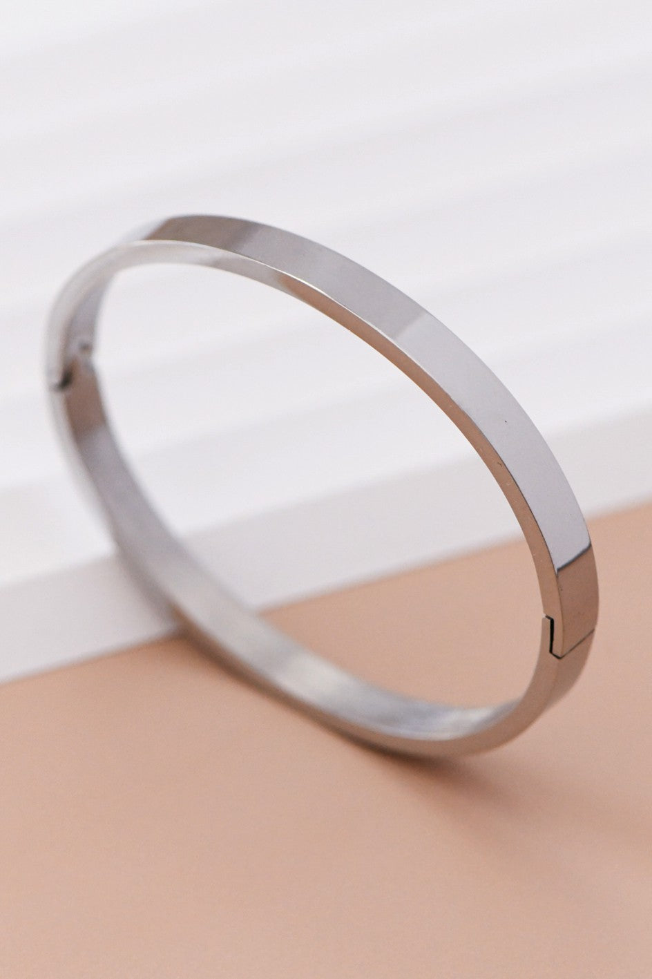 18k silver-plated stainless steel bangle bracelet on a beige surface with a light background