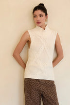 Woman wearing a cream mock neck knitted sleeveless top against a beige background