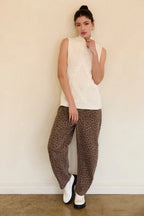 Woman wearing a cream mock neck knitted sleeveless top with brown pants against a beige background