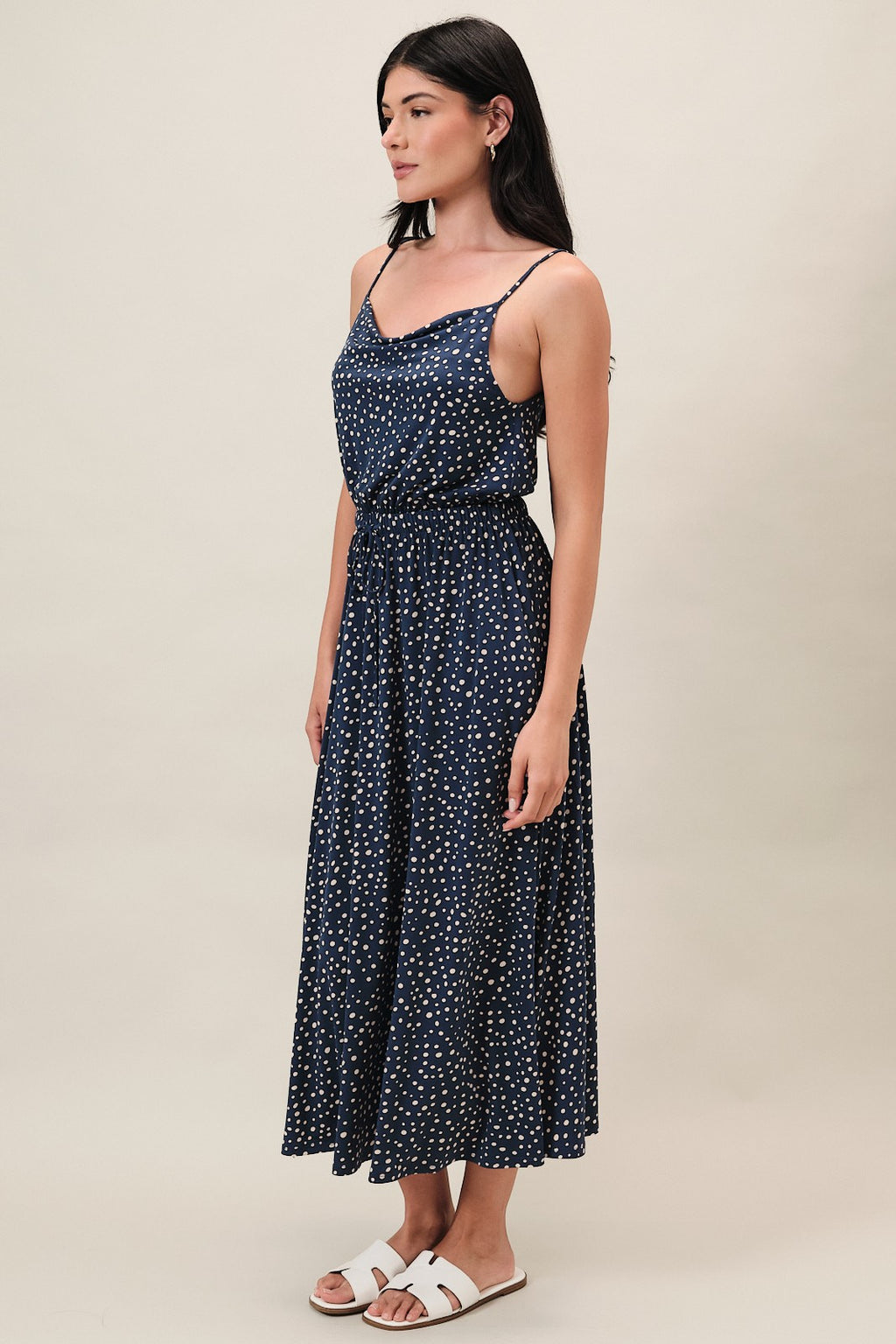 Woman wearing a navy dress with ivory polka dots on a beige background
