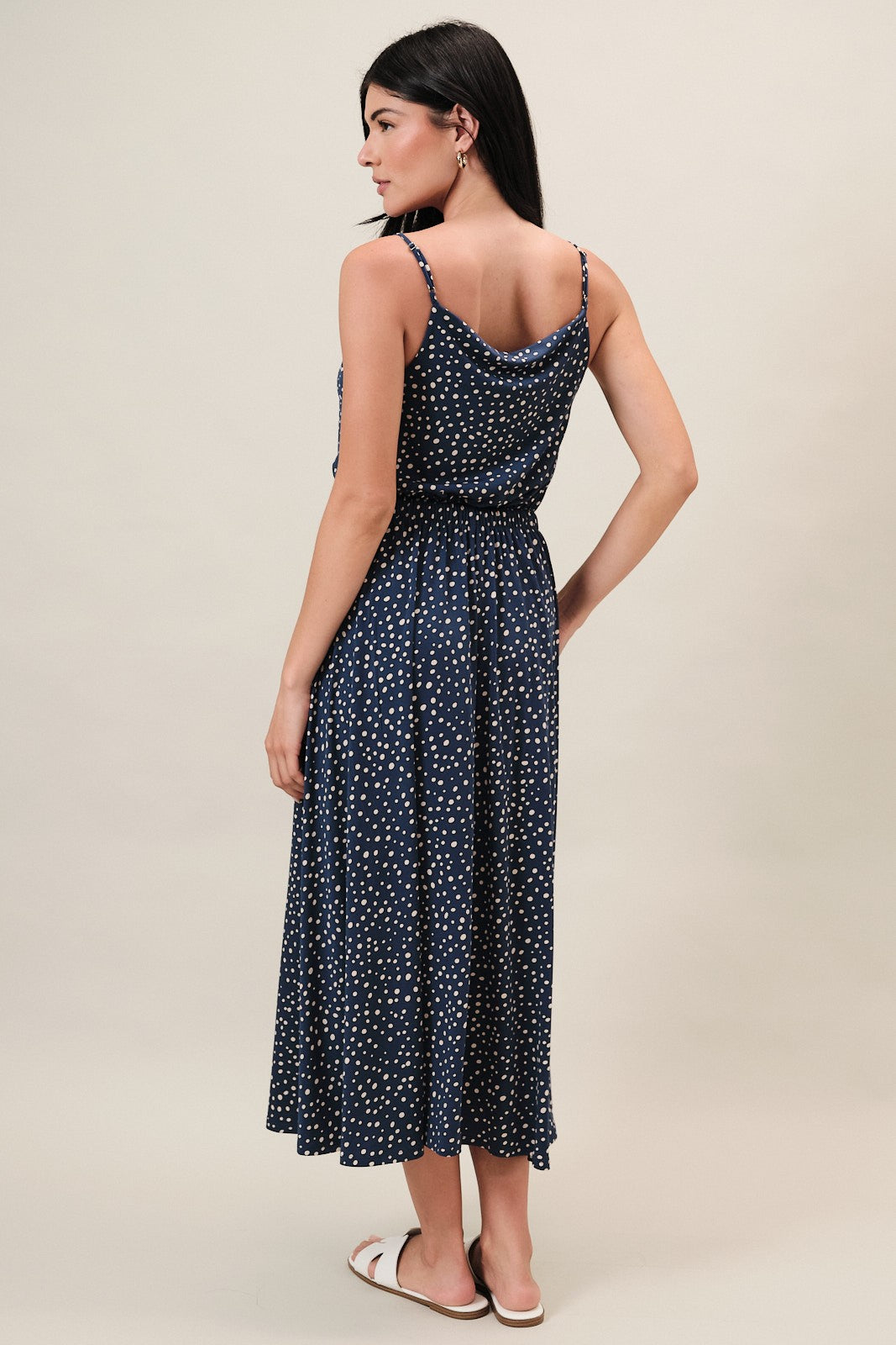 Woman wearing a navy dress with ivory polka dots on a beige background