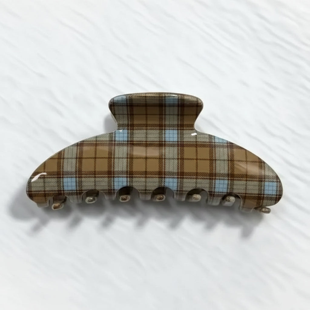 Hair claw with a brown, beige, and light blue plaid pattern, displayed on a textured white surface 