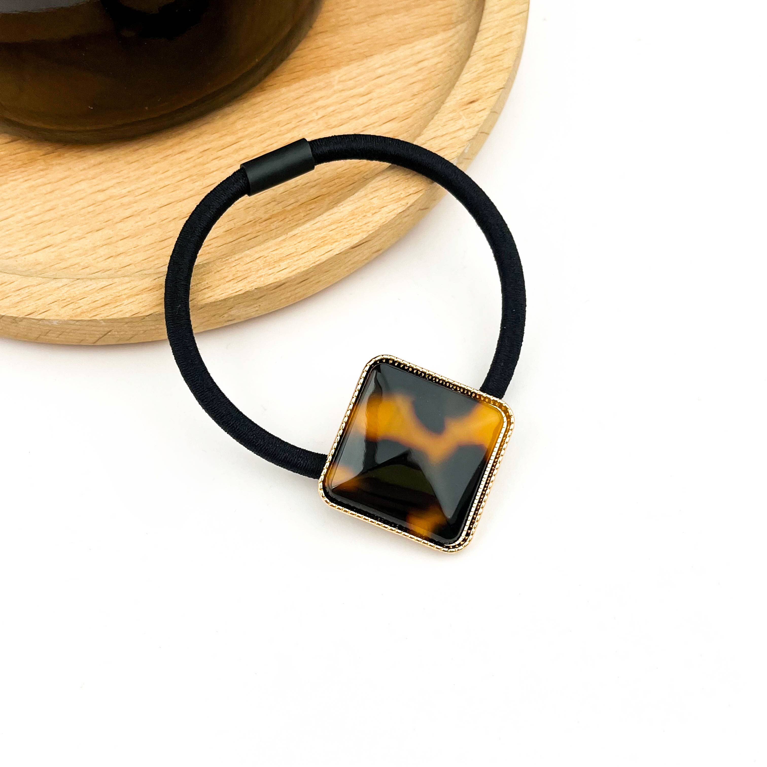 Black hair elastic with tortoiseshell square clip on a white background