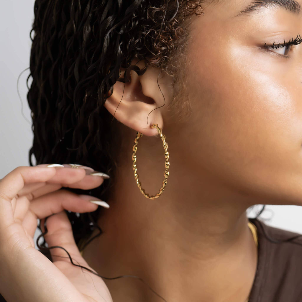 Close-up of a woman wearing a gold twisted hoop earring with a neutral background