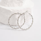 Silver twisted hoop earrings on a white fabric background