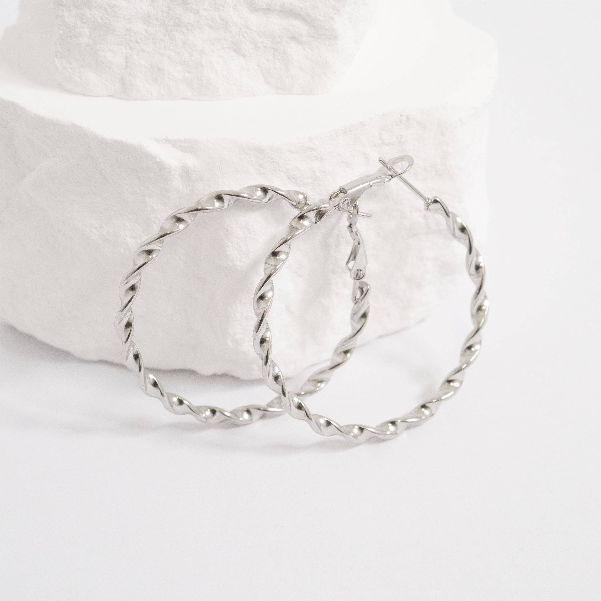 Silver twisted hoop earrings on a white fabric background