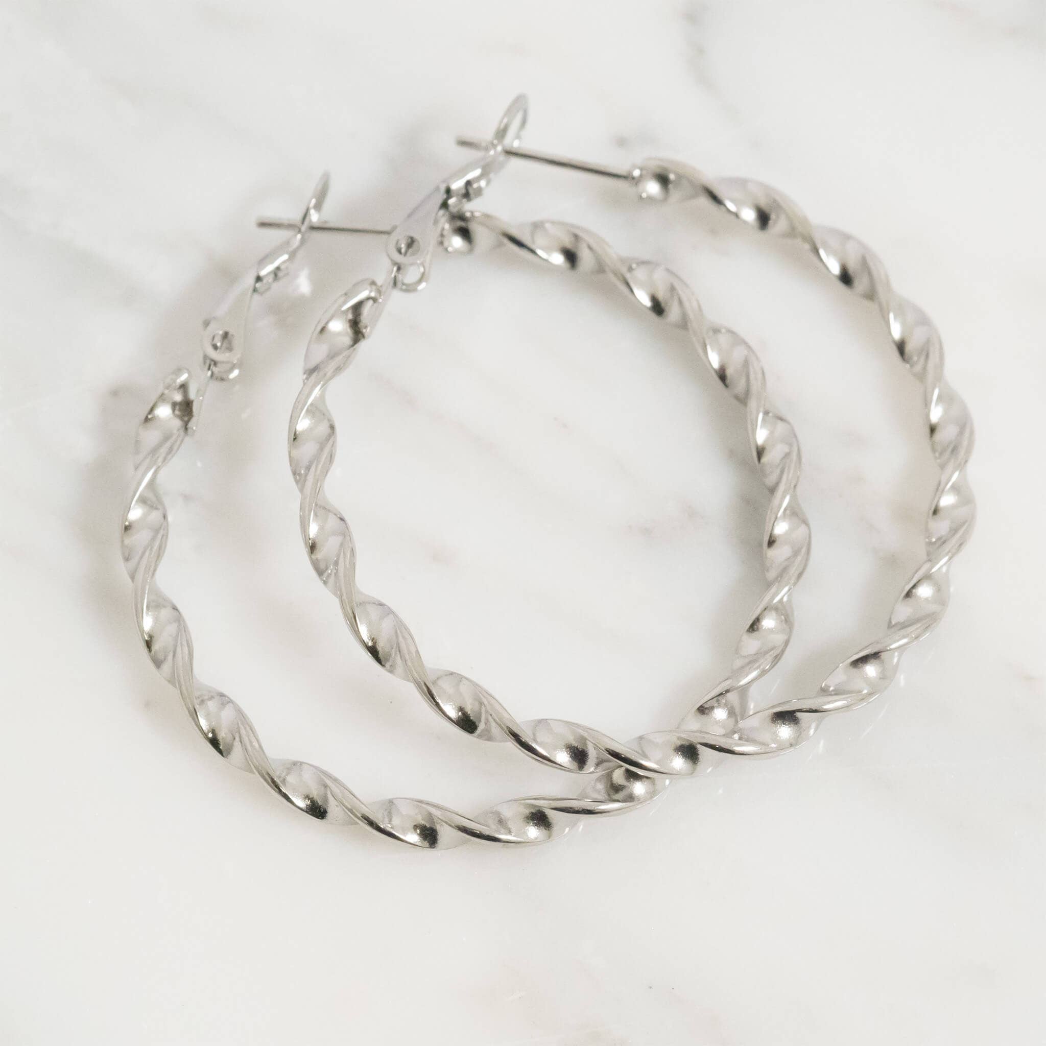 Pair of silver twisted hoop earrings on a white background