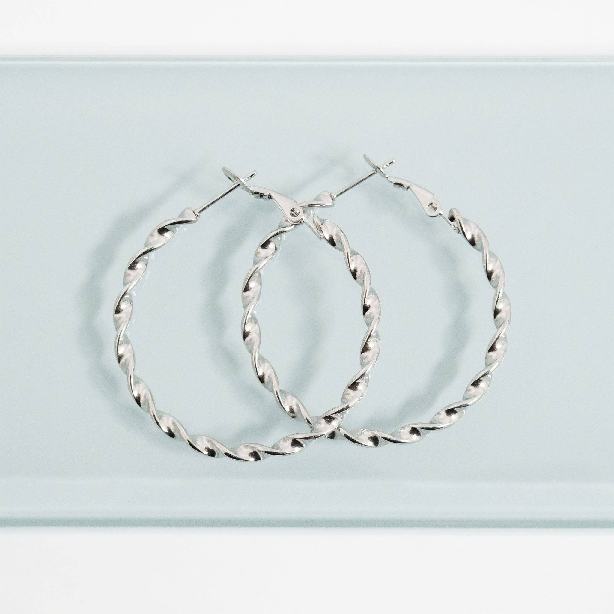 Silver twisted hoop earrings on a light blue background