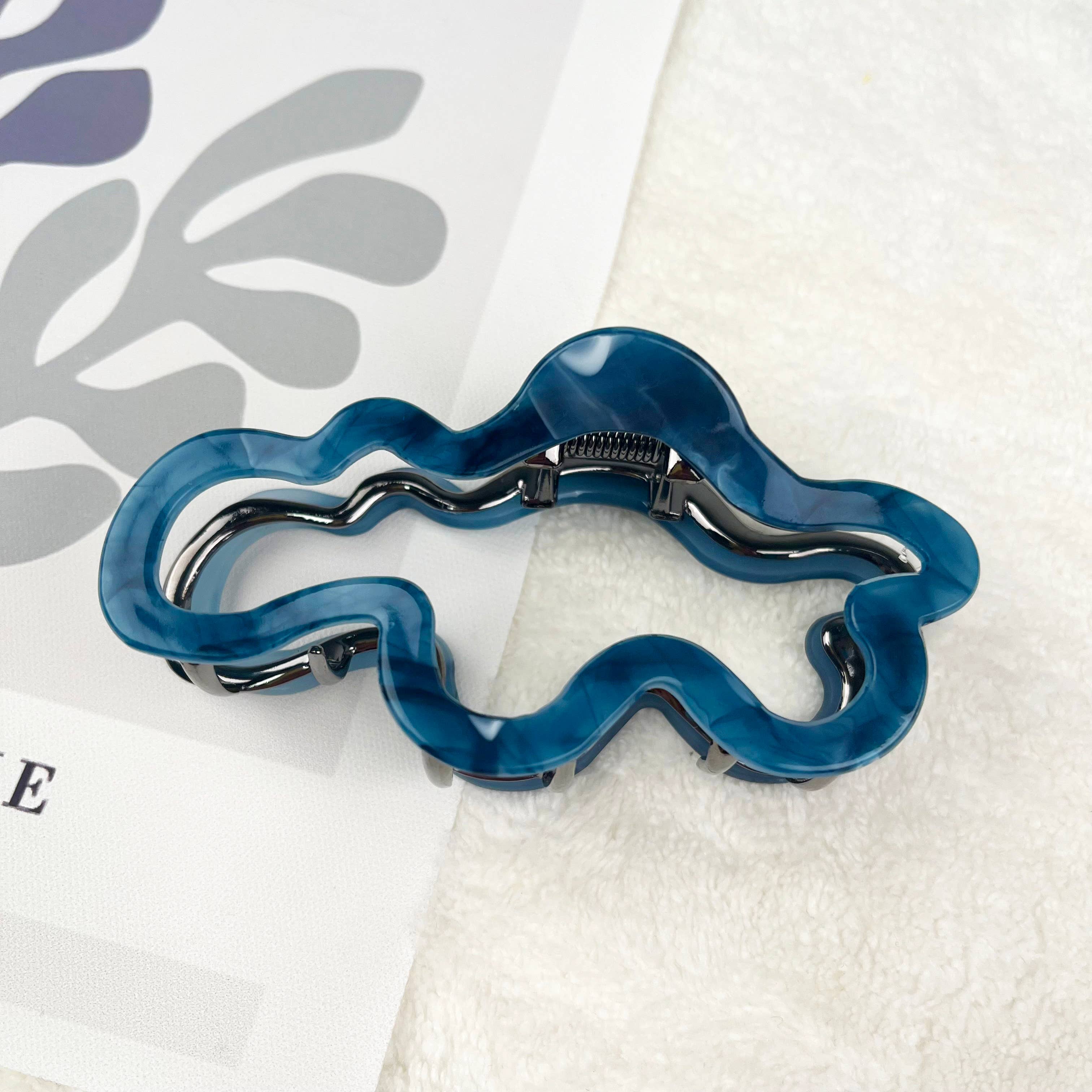 Blue cloud design hair claw clip on a textured white surface with leaf pattern
