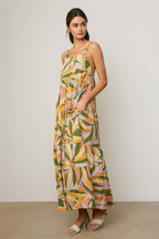 Woman wearing a colorful tropical design maxi dress against a neutral background