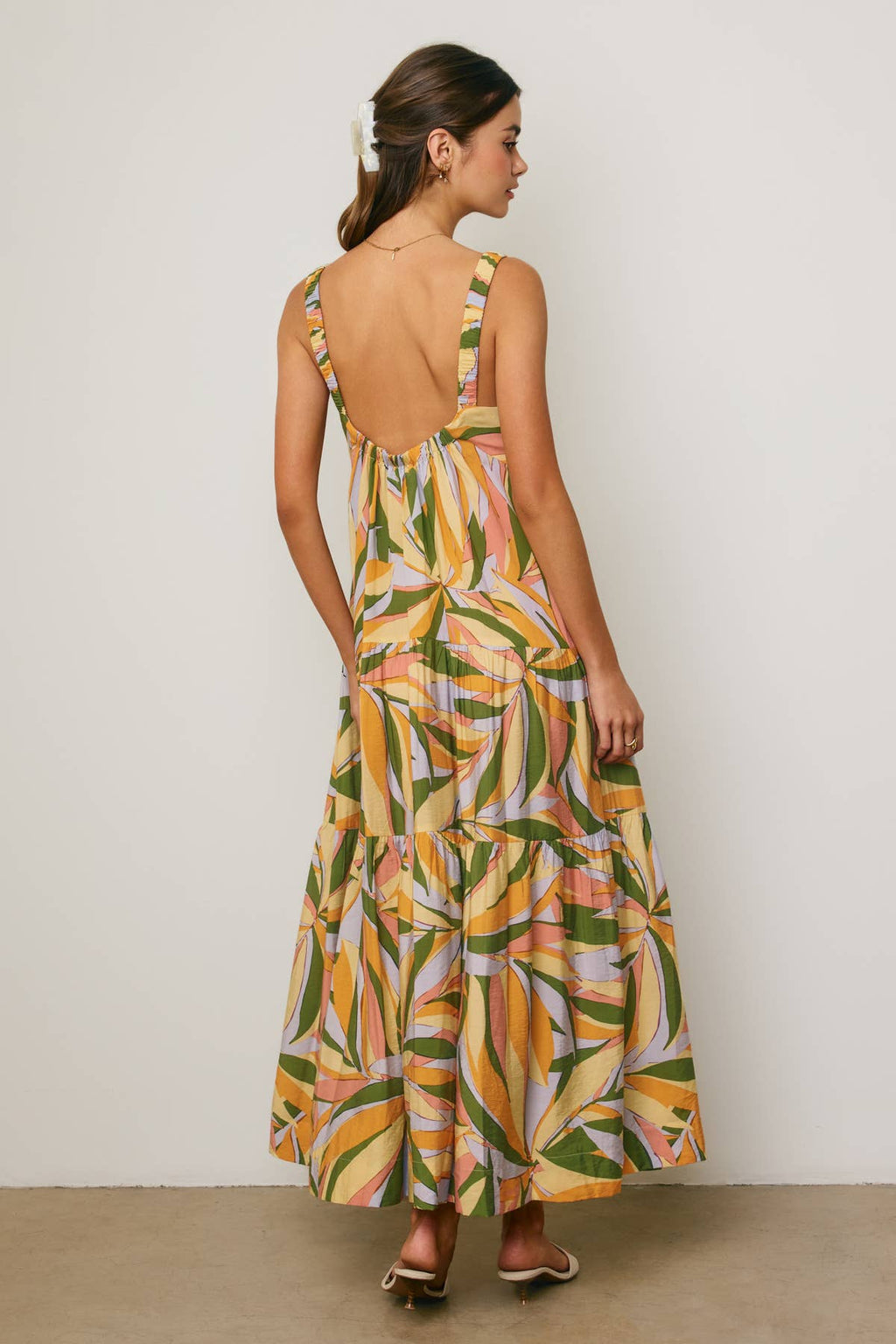 Back view of a woman wearing a colorful tropical design maxi dress against a neutral background