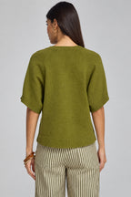 A woman shown from the back wearing a short-sleeve knit top in olive green and striped pants, photographed against a plain gray studio background.