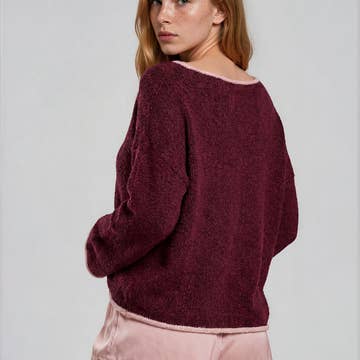 Back view of a woman wearing a burgundy boat neck sweater with pink roll up trim and pink lace shorts on a plain background
