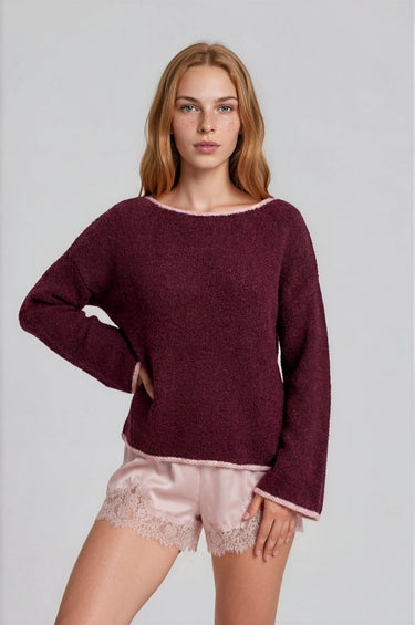 Woman wearing a burgundy boat neck sweater with pink roll up trim and pink lace shorts on a plain background