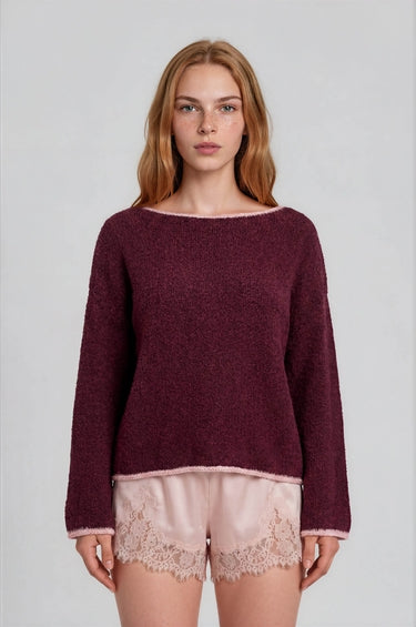 Woman wearing a burgundy boat neck sweater with pink roll up trim and pink lace shorts on a plain background