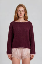 Woman wearing a burgundy boat neck sweater with pink roll up trim and pink lace shorts on a plain background