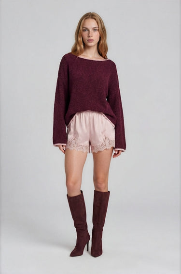 Woman wearing a burgundy boat neck sweater with pink roll up trim and pink lace shorts on a plain background