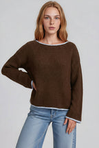 A woman modeling a brown long-sleeve sweater with light blue trimagainst a light gray studio background.