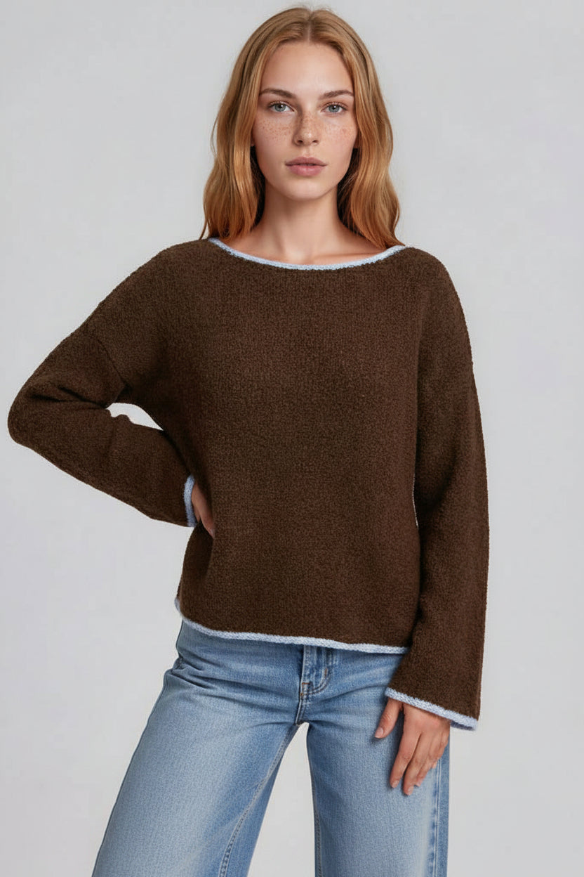 A woman modeling a brown long-sleeve sweater with light blue trimagainst a light gray studio background.