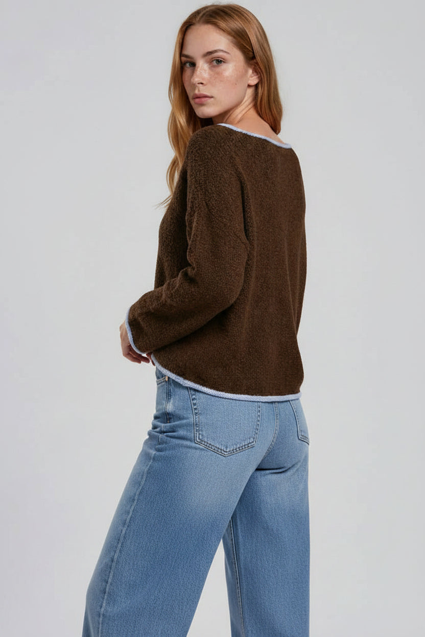 Back view of a woman modeling a brown long-sleeve sweater with light blue trim, paired with light pink satin shorts with lace trim, against a light gray studio background.