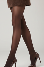 A model's legs wearing a textured gray mini skirt, sheer dark brown tights, and black patent high heels against a white studio background.