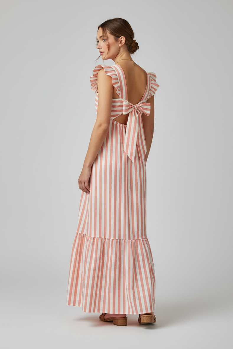 Woman wearing a coral and cream striped dress with a back bow detail on a plain background.
