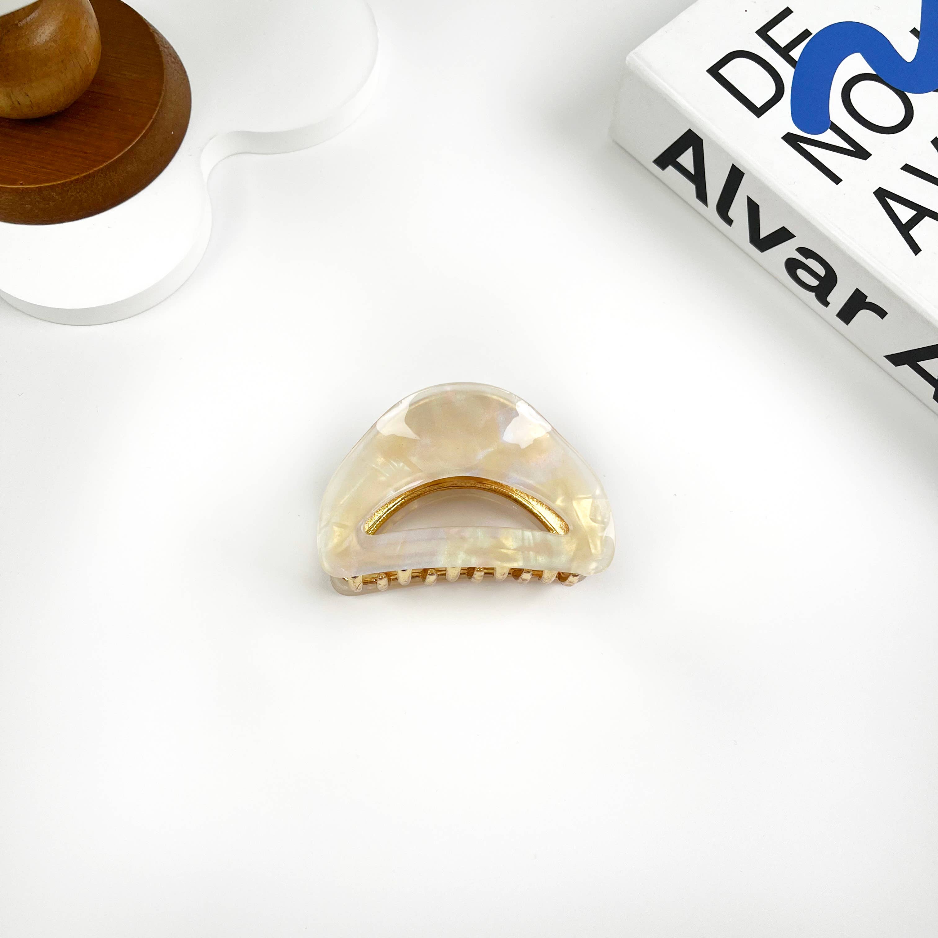 Beige hair claw clip on a white surface with a book in the background