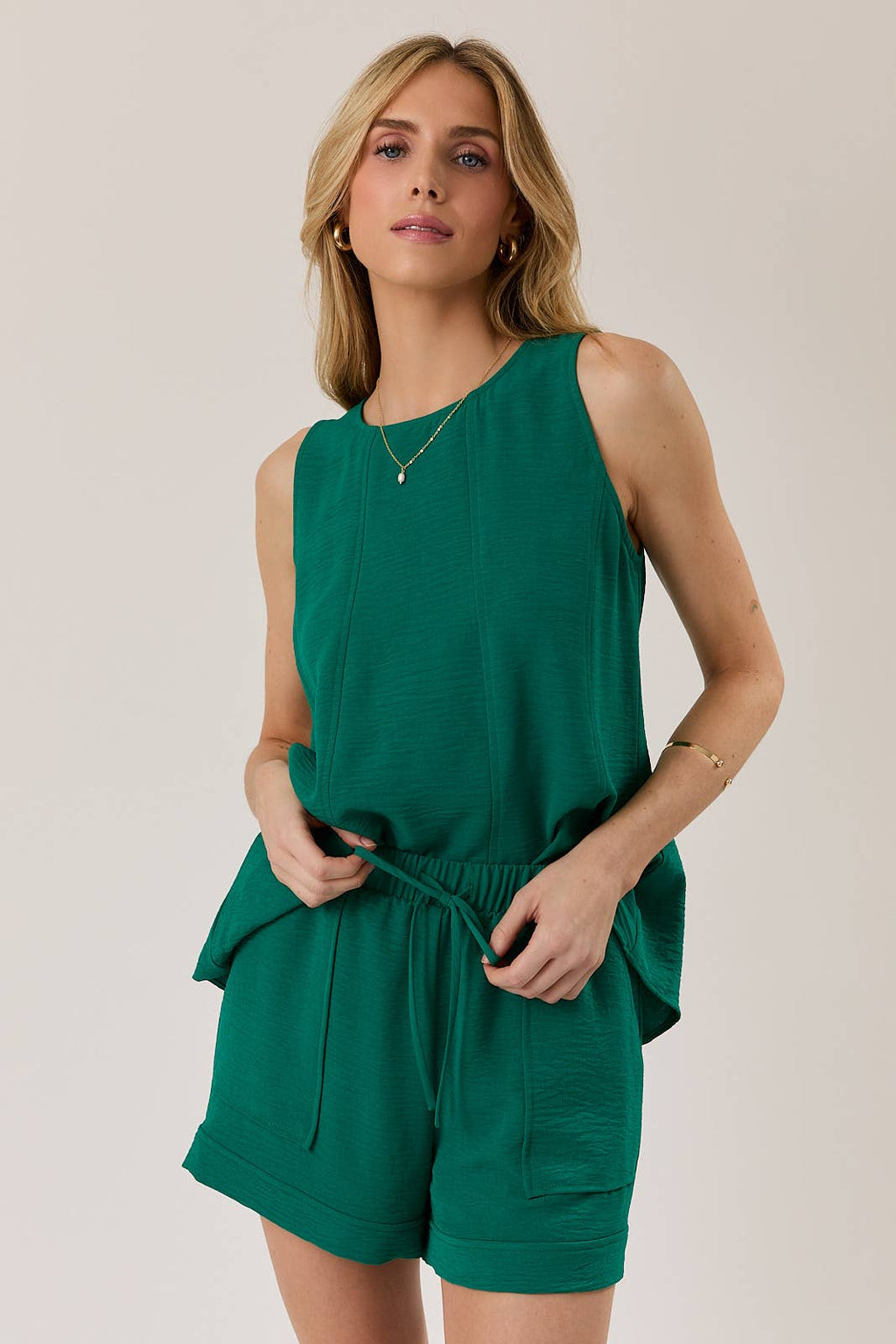 Woman wearing a hunter green tank top and shorts against a plain background