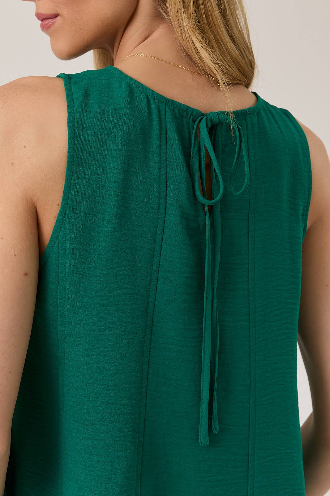 Back view of a woman wearing a hunter green tank top with tie back against a plain background