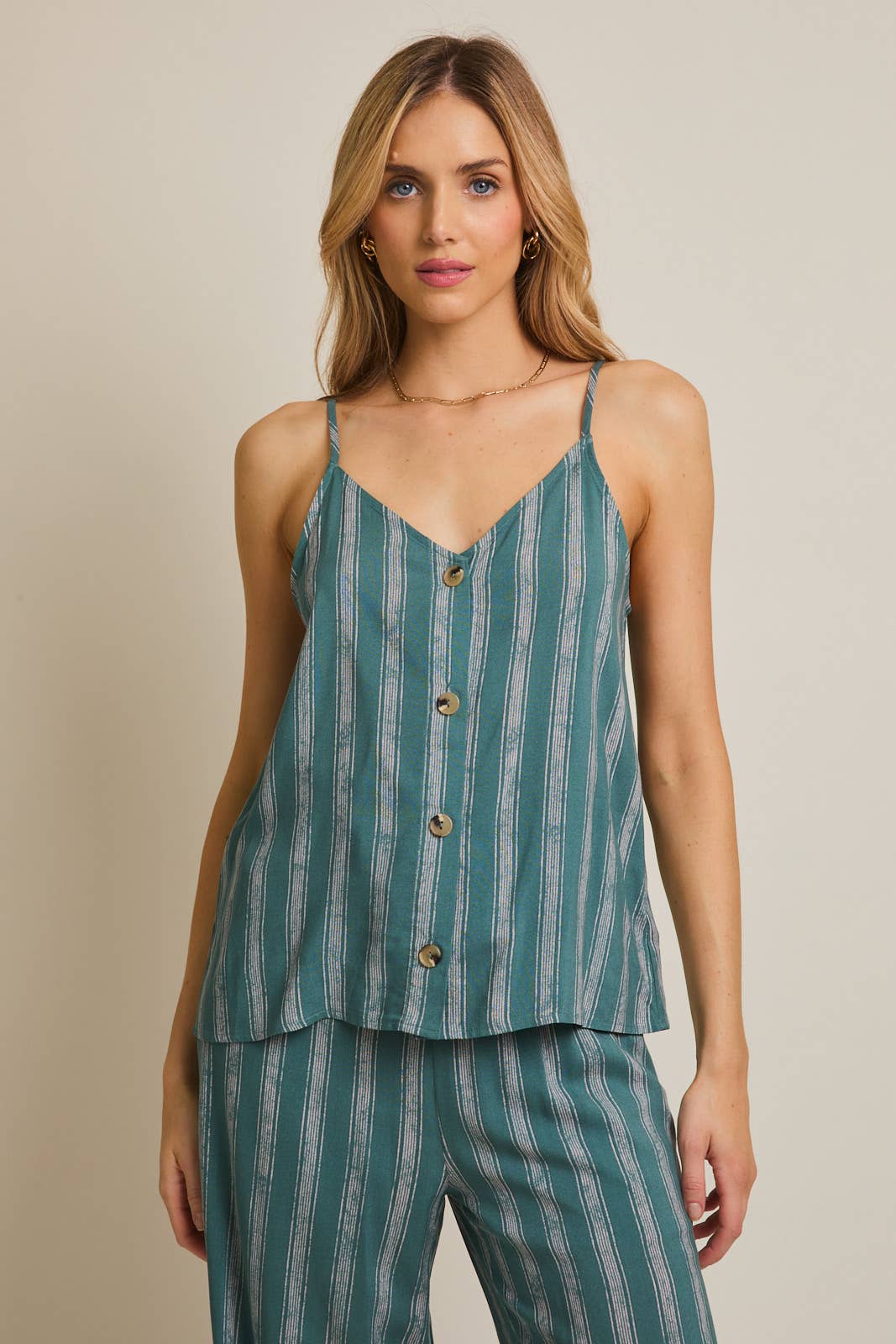 Woman wearing green and cream striped spaghetti strap top on gray background